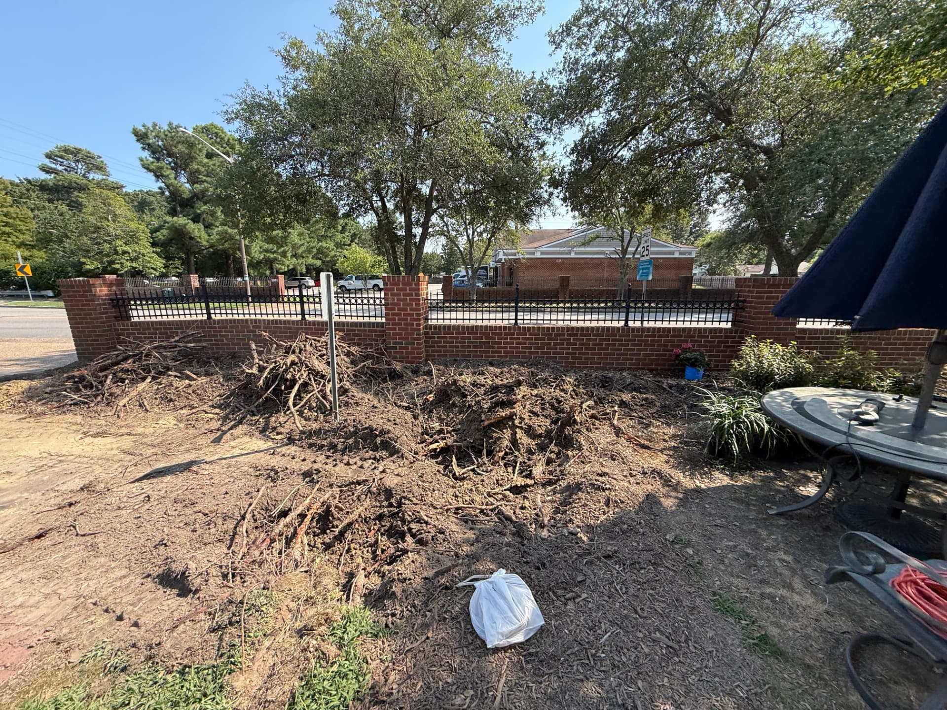 Beds churned to bare soil with piles of roots and cleared debris along a brick wall, before the mulch refresh
