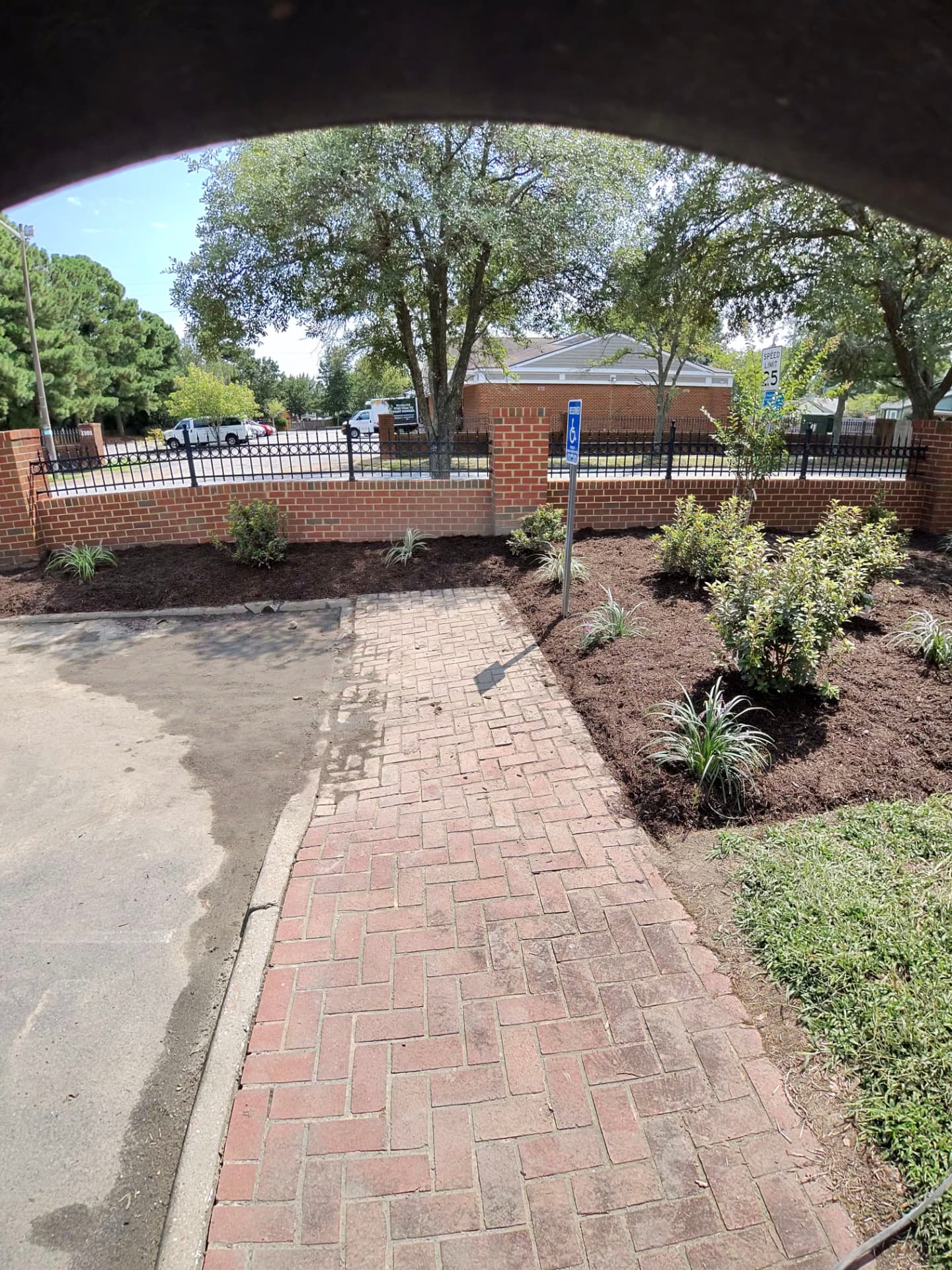 The same beds along the brick wall finished with fresh dark mulch, new shrubs and ornamental plantings beside a brick walkway
